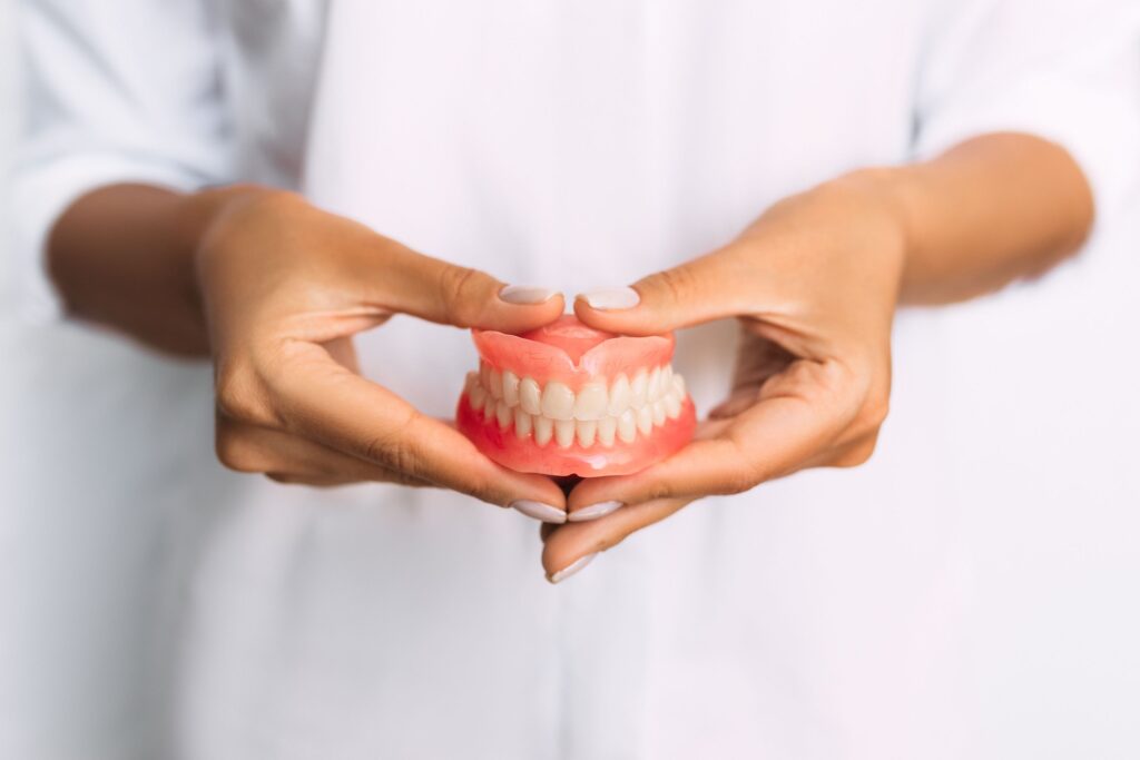 Dentist in white jacket holding full set of dentures in front of midsection